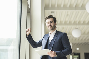 Successful manager standing in modern office building, using laptop - UUF17764