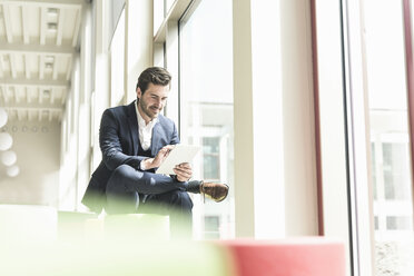 Young businessman sitting in lounge, using digital tablet - UUF17772