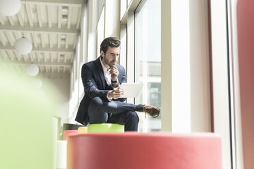 Young businessman sitting in lounge, using digital tablet - UUF17774