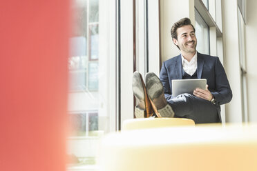 Young businessman sitting in lounge, using digital tablet - UUF17780