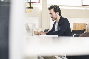 Young businessman sitting in office, using laptop - UUF17786