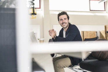 Junger Geschäftsmann sitzt im Büro und benutzt einen Laptop - UUF17788