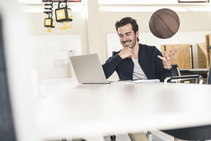 Junger Geschäftsmann mit Laptop, der mit einem Basketball spielt - UUF17796
