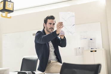 Young businessman in office holding foil of a blueprint - UUF17799