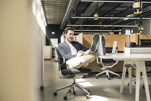 Junger Geschäftsmann arbeitet entspannt in einem modernen Büro und macht sich Notizen - UUF17804