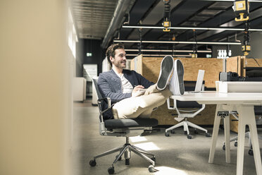 Junger Geschäftsmann arbeitet entspannt in einem modernen Büro und macht sich Notizen - UUF17805