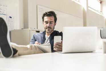 Young businessman working relaxed in modern office using smartphone and laptop, - UUF17807