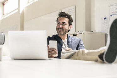 Young businessman working relaxed in modern office using smartphone and laptop, - UUF17808