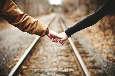 Nahaufnahme eines sich an den Händen haltenden Paares auf Bahngleisen - BLEF06320