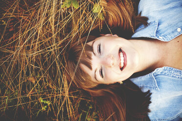 Nahaufnahme einer lächelnden Frau, die im hohen Gras liegt - BLEF06328