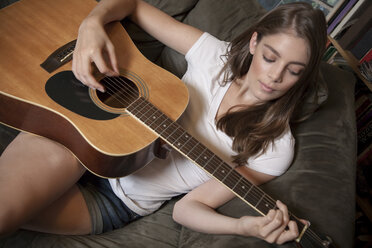 Caucasian woman playing guitar on sofa - BLEF06338