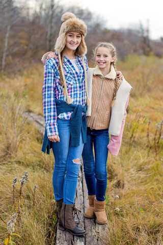 Lächelnde Schwestern auf einem Holzsteg in einem Feld, lizenzfreies Stockfoto
