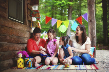 Drei Generationen von kaukasischen Frauen spielen mit Spielzeug auf der Veranda einer Hütte - BLEF06438