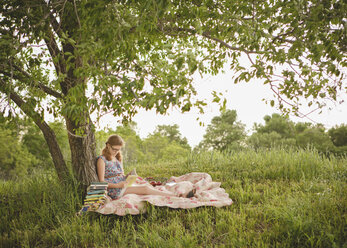 Kaukasisches Mädchen, das unter einem Baum auf einem Feld ein Buch liest - BLEF06464