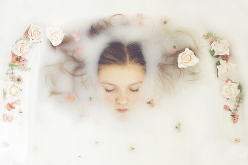 Caucasian teenage girl floating in milk bath with flowers - BLEF06478