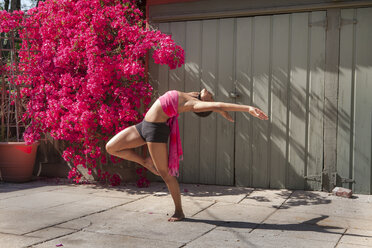 Frau übt Yoga in der Nähe von Blumen und Zaun - BLEF06493