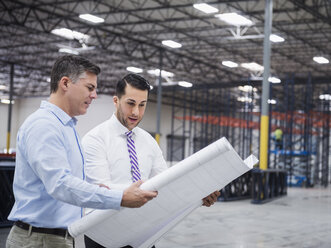 Caucasian architects reading blueprints in warehouse - BLEF06578