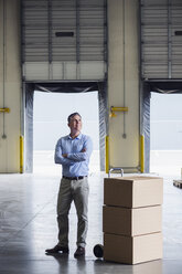 Caucasian businessman standing near cardboard boxes in warehouse - BLEF06579