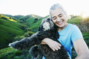 Older Caucasian woman hugging dog on rural hilltop - BLEF06594