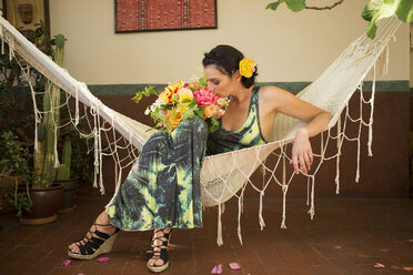 Woman smelling bouquet of flowers in hammock - BLEF06617