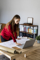 Frau im Büro arbeitet an einem Plan und Laptop mit einem Windkraftanlagenmodell auf dem Tisch - GIOF06389