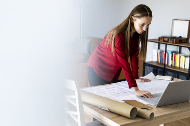 Frau im Büro arbeitet an einem Plan und Laptop auf dem Tisch - GIOF06390