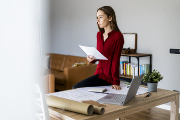 Woman in office holding paper with wind turbine model on table - GIOF06397