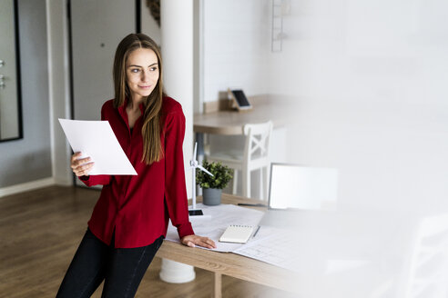 Frau im Büro hält Papier mit Windradmodell auf dem Tisch - GIOF06399