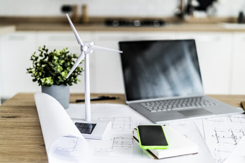 Modell einer Windkraftanlage, Bauplan, Handy und Laptop auf einem Tisch im Büro - GIOF06404