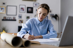 Frau im Büro macht sich Notizen mit Plan und Laptop auf dem Tisch - GIOF06410