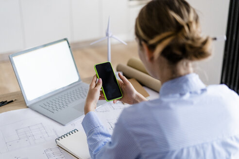 Frau im Büro mit Handy und Windradmodell auf dem Tisch - GIOF06415