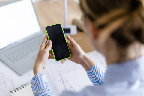 Nahaufnahme einer Frau im Büro, die ein Mobiltelefon mit einem Windradmodell auf dem Tisch benutzt, lizenzfreies Stockfoto