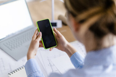 Close-up of woman in office using cell phone with wind turbine model on table - GIOF06416