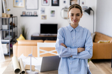 Portrait of confident woman standing in office with wind turbine model on table - GIOF06418