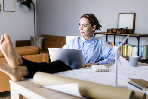 Frau im Büro arbeitet am Laptop mit den Füßen auf dem Tisch - GIOF06422