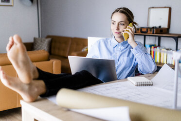 Woman in office on cell phone with feet on table - GIOF06423