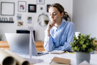 Woman with closed eyes in office with wind turbine model on table - GIOF06428