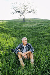 Older Caucasian man sitting on grassy hillside - BLEF06646