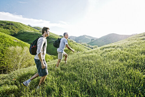 Caucasian father and son walking on grassy hillside - BLEF06648