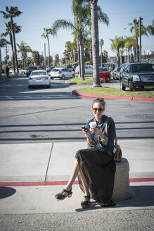 Caucasian woman sitting on concrete barrier in parking lot - BLEF06673
