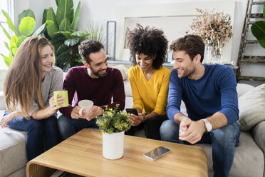 Four happy friends sitting on couch using cell phone - GIOF06439