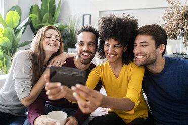 Four happy friends sitting on couch taking a selfie - GIOF06442