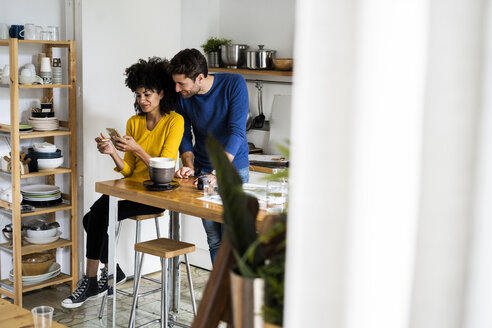 Couple in kitchen at home sharing cell phone - GIOF06458