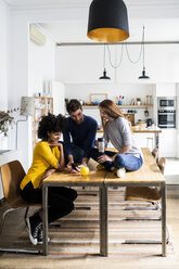 Three friends sharing cell phone on dining table at home - GIOF06472