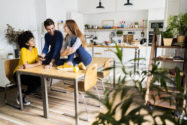 Three happy friends with cell phone on dining table at home - GIOF06473