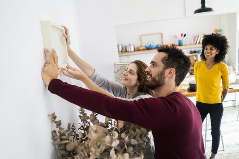 Friends hanging up picture frame at home - GIOF06475