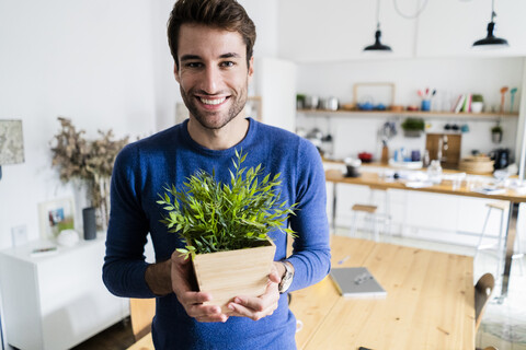 Porträt eines lächelnden jungen Mannes, der eine Pflanze zu Hause hält, lizenzfreies Stockfoto