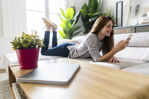 Lächelnde Frau auf der Couch liegend mit Mobiltelefon, lizenzfreies Stockfoto