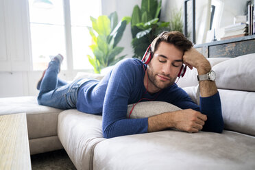 Relaxed man lying on couch listening to music - GIOF06489