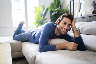 Relaxed man lying on couch listening to music - GIOF06490